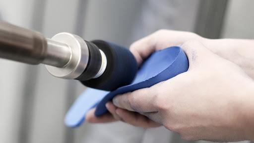 A close-up of hands cleaning an insole using a rotary tool with a black attachment