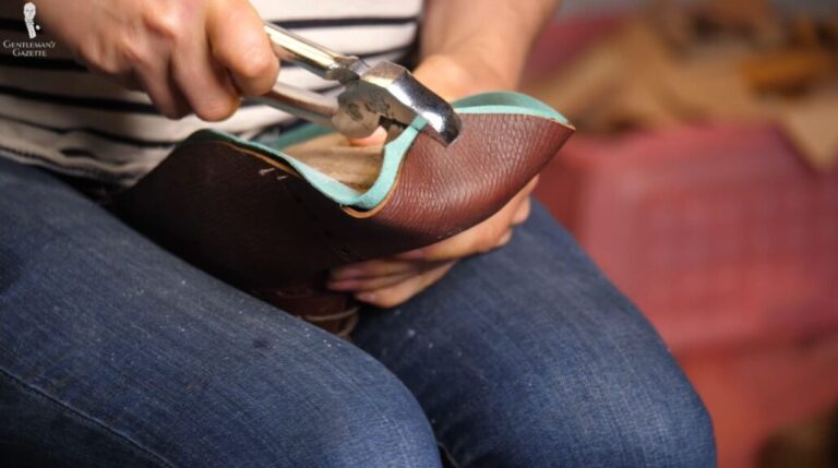 A person skillfully uses pliers to shape and craft a leather shoe, demonstrating craftsmanship and attention to detail