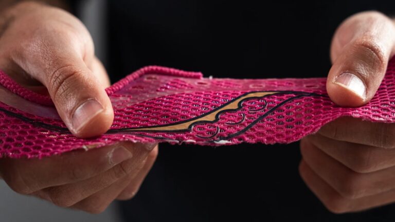 Close-up of a person holding a piece of red mesh fabric embedded with intricate black electronic circuitry