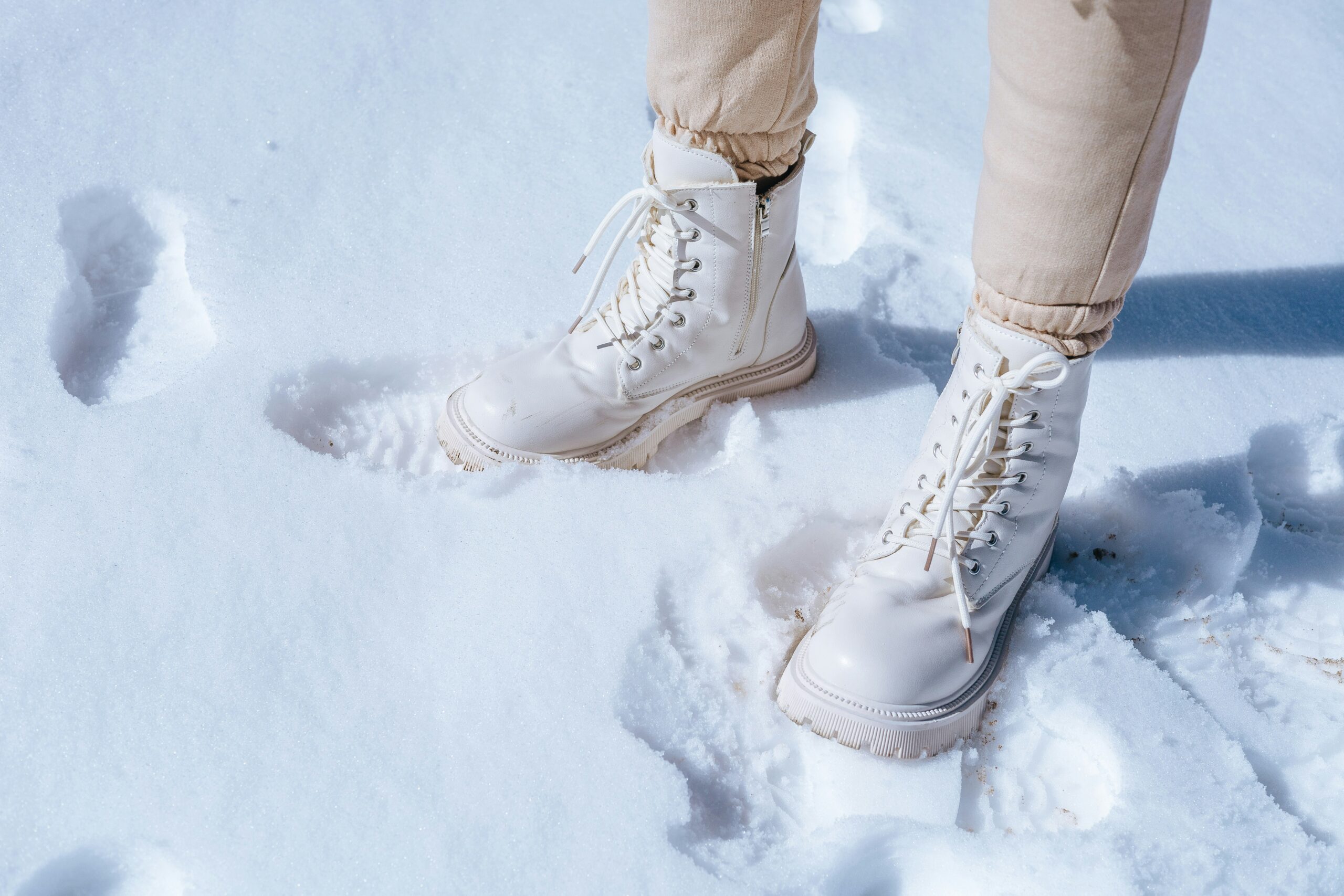 shows white boots leaving footprints in the snow emphasizing their temperature resistance in cold environments