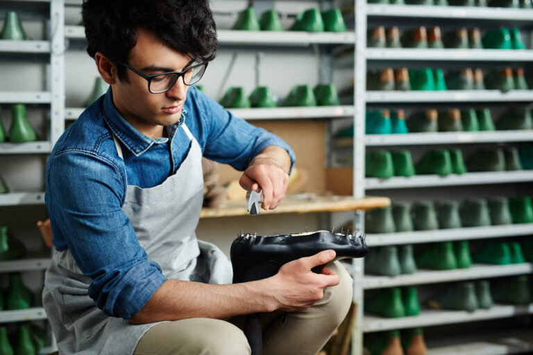 Young professional cobbler taking out nails from shoe workpiece in black leather for inventory control